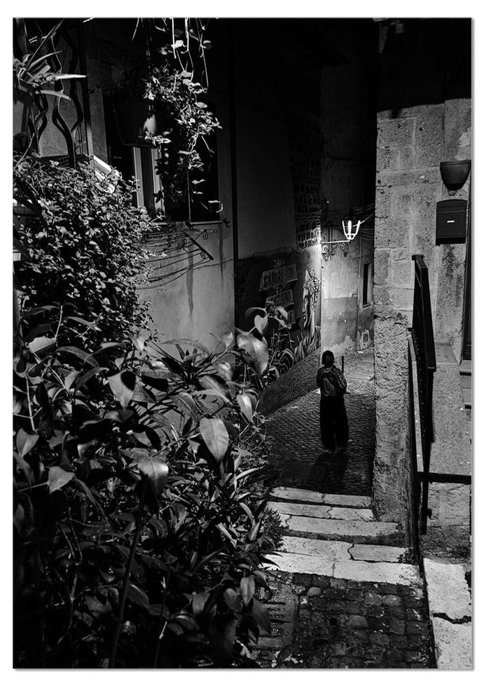 A Mezzanotte black and white fine art photograph of a solitary figure in a narrow Italian street at night
