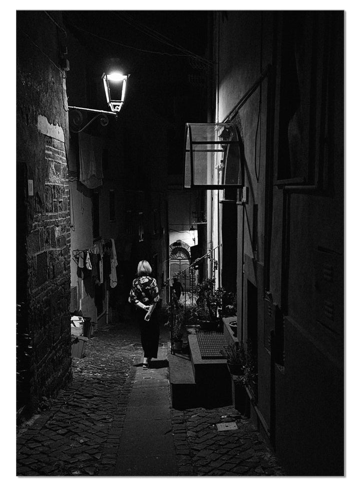 La Passeggiata black and white fine art photograph of a woman walking through a narrow Italian street at night