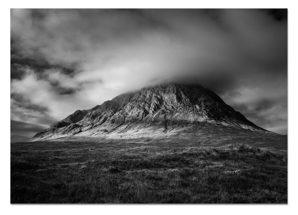 Black and white photograph of Buachaille Etive Mòr in Glencoe, with dramatic storm clouds gathering over the mountain and light breaking across its slopes.