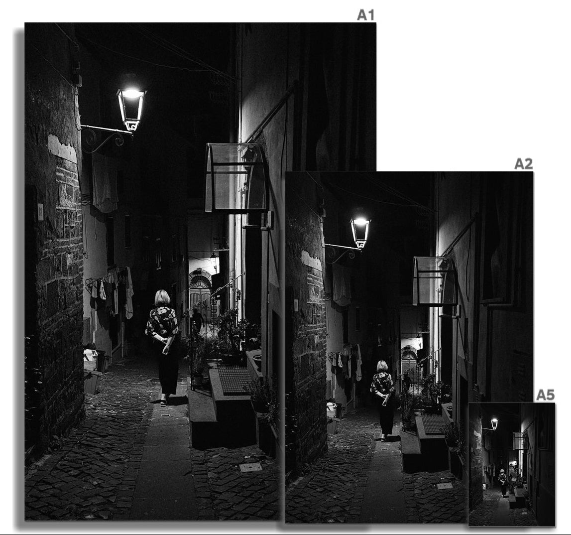 La Passeggiata black and white fine art photograph of a woman walking through a narrow Italian street at night