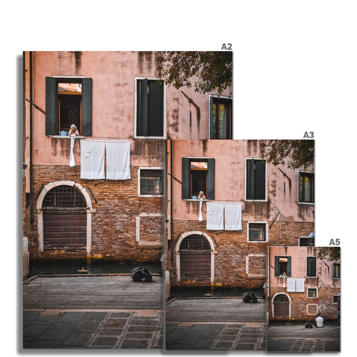 Two Strangers in Venice fine art photograph showing an elderly woman leaning from a Venetian window while a lone figure sits beside a quiet canal below.